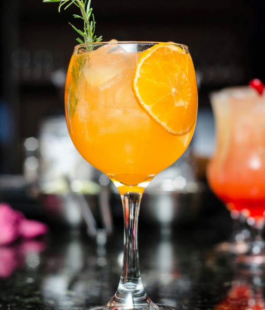 Oranger Cocktail mit Eiswürfeln, Orangenscheibe und Rosmarin im Wirtshaus Ausspann´