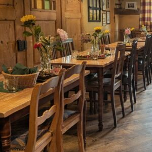 Rustikaler Gastraum mit langen Holztischen, Stühlen und Blumendekoration im Wirtshaus Ausspann´