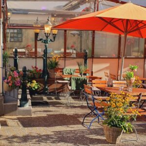 Sonniger Biergarten mit Holztischen, großem Sonnenschirm und Blumendekoration im Wirtshaus Ausspann´