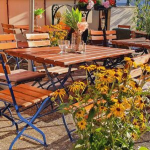 Sonniger Biergarten mit Holztischen, Stühlen und gelben Blumen im Wirtshaus Ausspann´